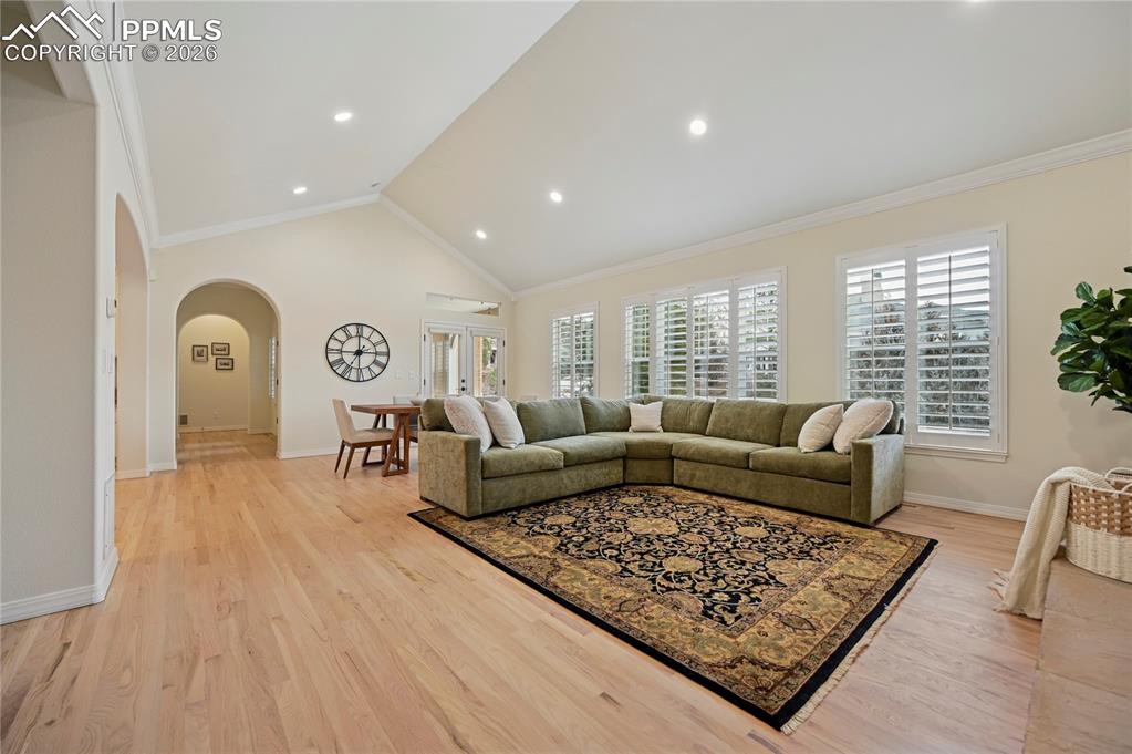 Image 16 of 50: Living area with arched walkways, crown molding, light wood-style floors, v