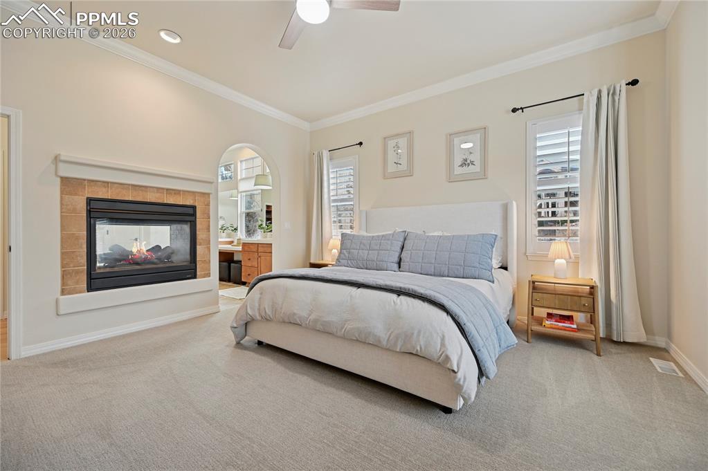 Image 19 of 50: Bedroom with carpet, a multi sided fireplace, multiple windows, ornamental 