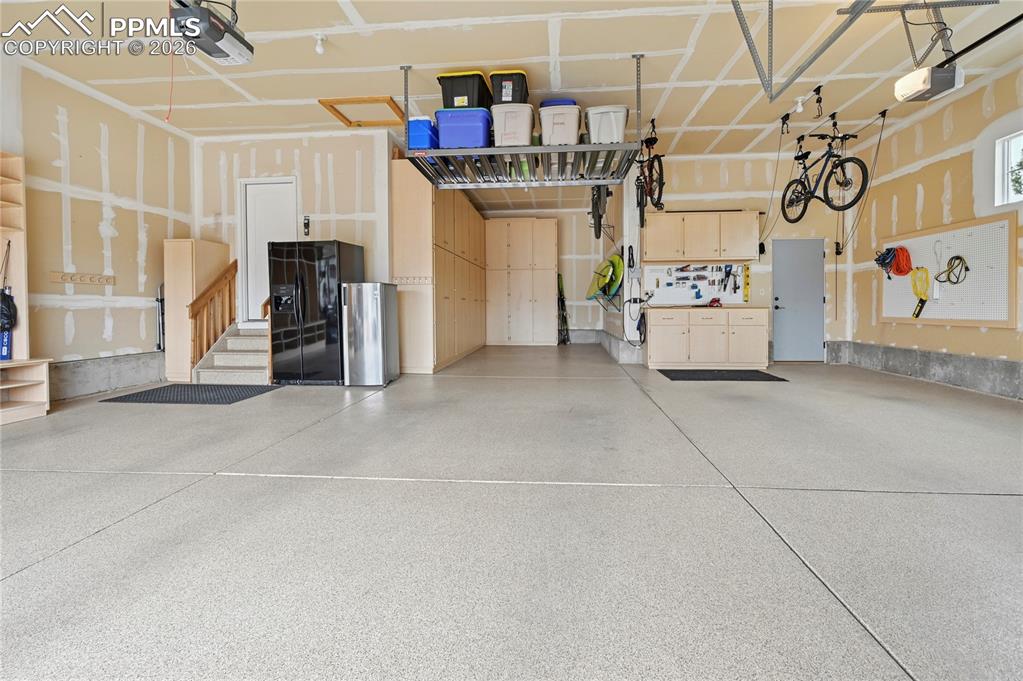 Image 44 of 50: Garage featuring black fridge with ice dispenser and a garage door opener