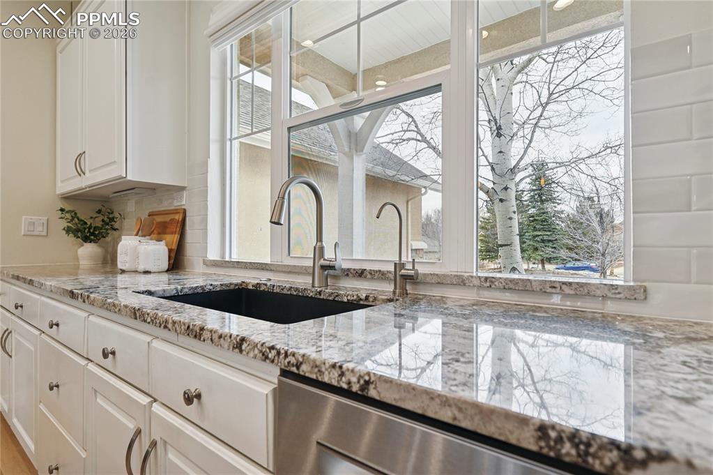 Image 8 of 50: Kitchen featuring light stone counters, white cabinetry, and dishwasher