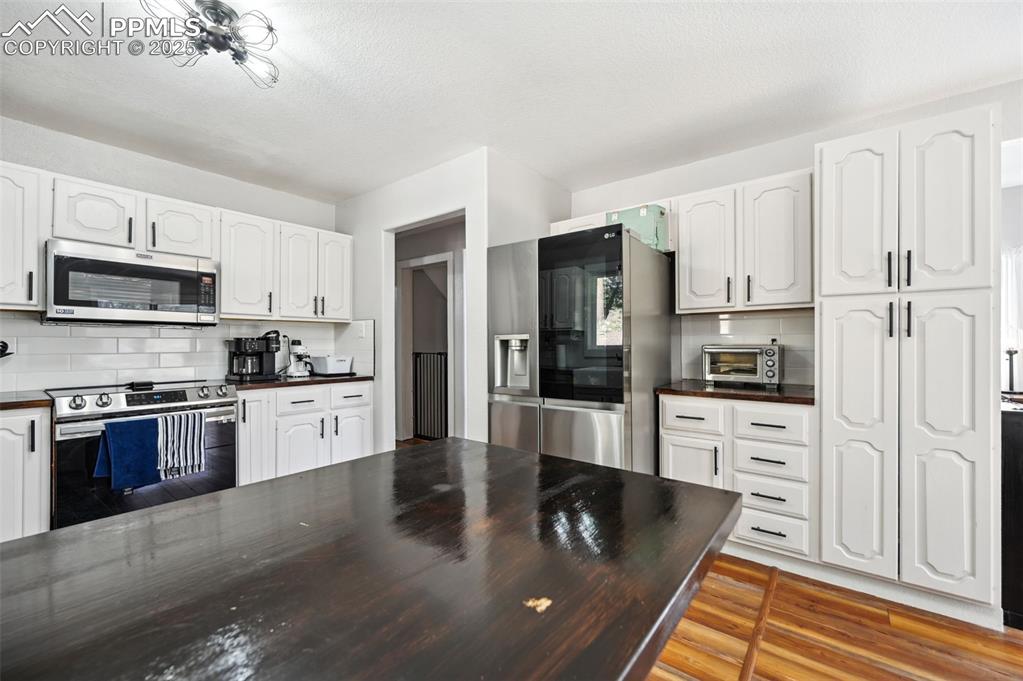 Image 12 of 49: Kitchen with stainless steel appliances, white cabinetry, backsplash, light