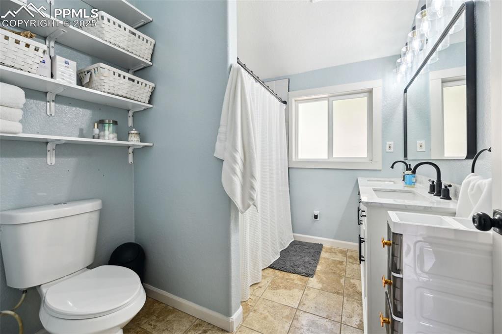 Image 20 of 49: Bathroom with double vanity, a shower with curtain, and stone finish floori