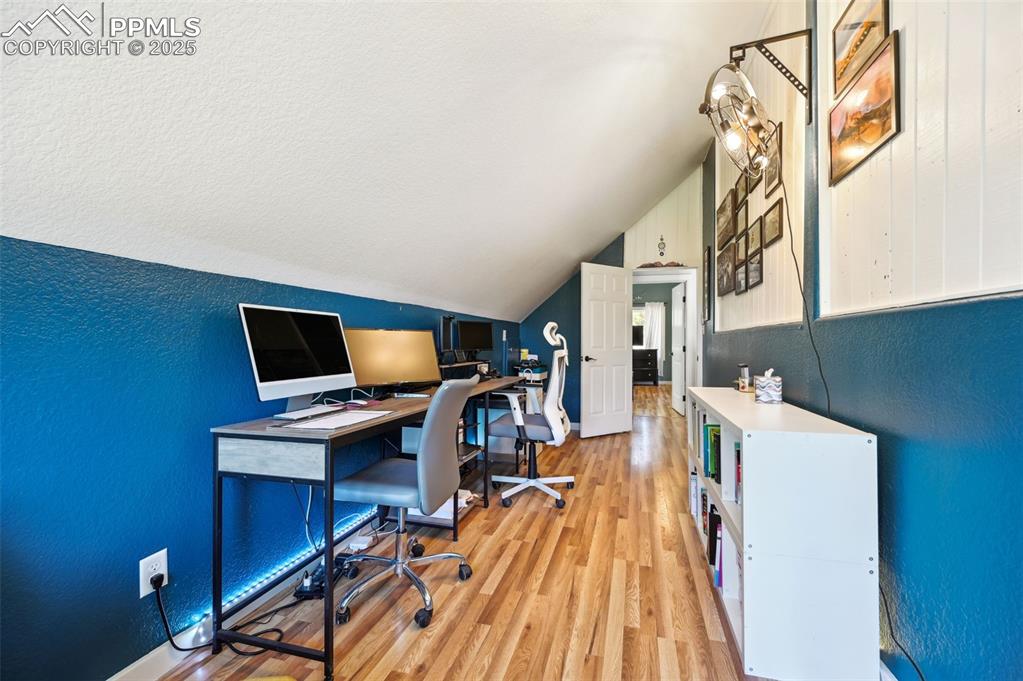 Image 22 of 49: Office area featuring a textured wall, lofted ceiling, and light wood-style