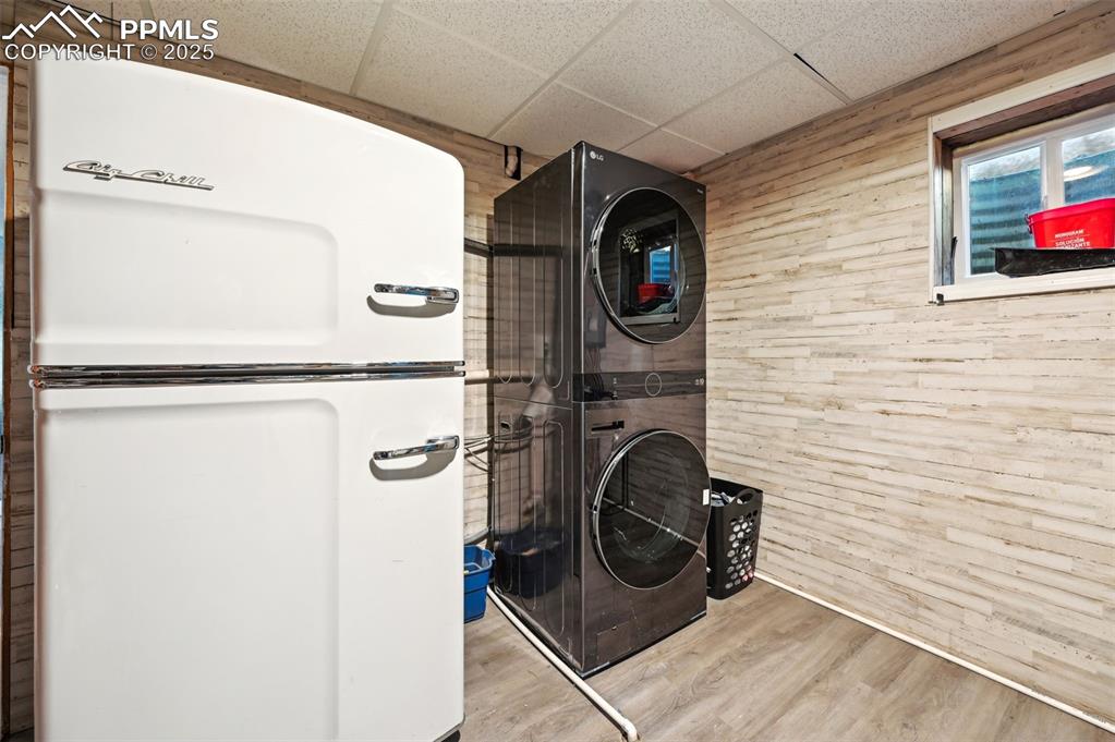 Image 37 of 49: Washroom with stacked washing machine and dryer, wooden walls, and wood fin