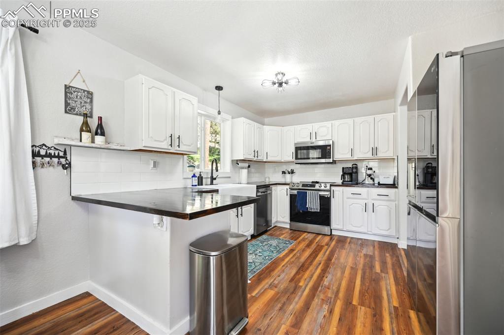 Image 8 of 49: Kitchen with stainless steel appliances, a peninsula, dark countertops, and