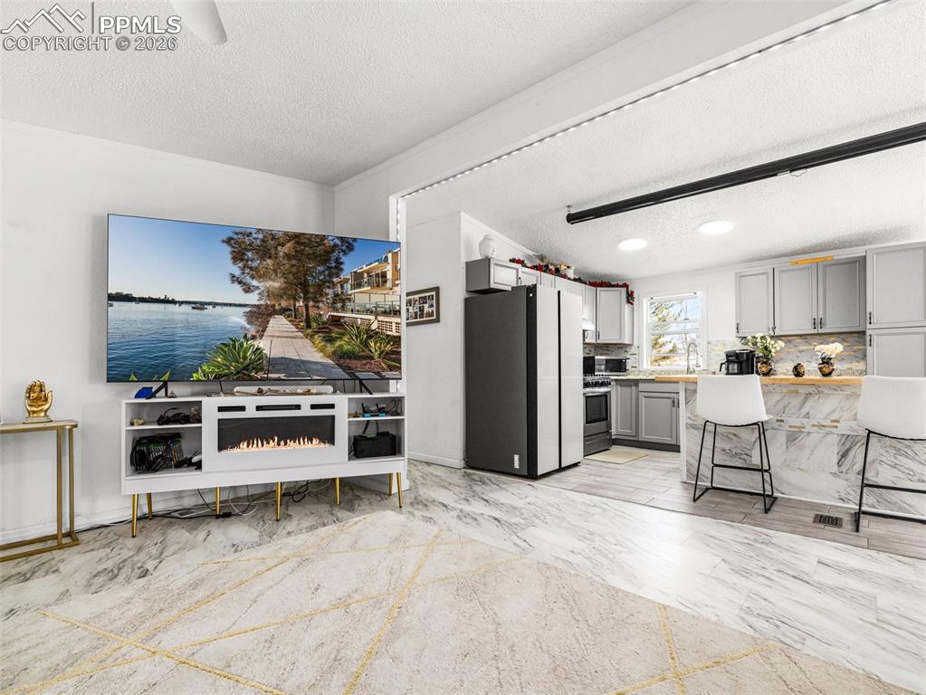 Image 10 of 29: Kitchen featuring gray cabinets, a kitchen bar, a textured ceiling, light c