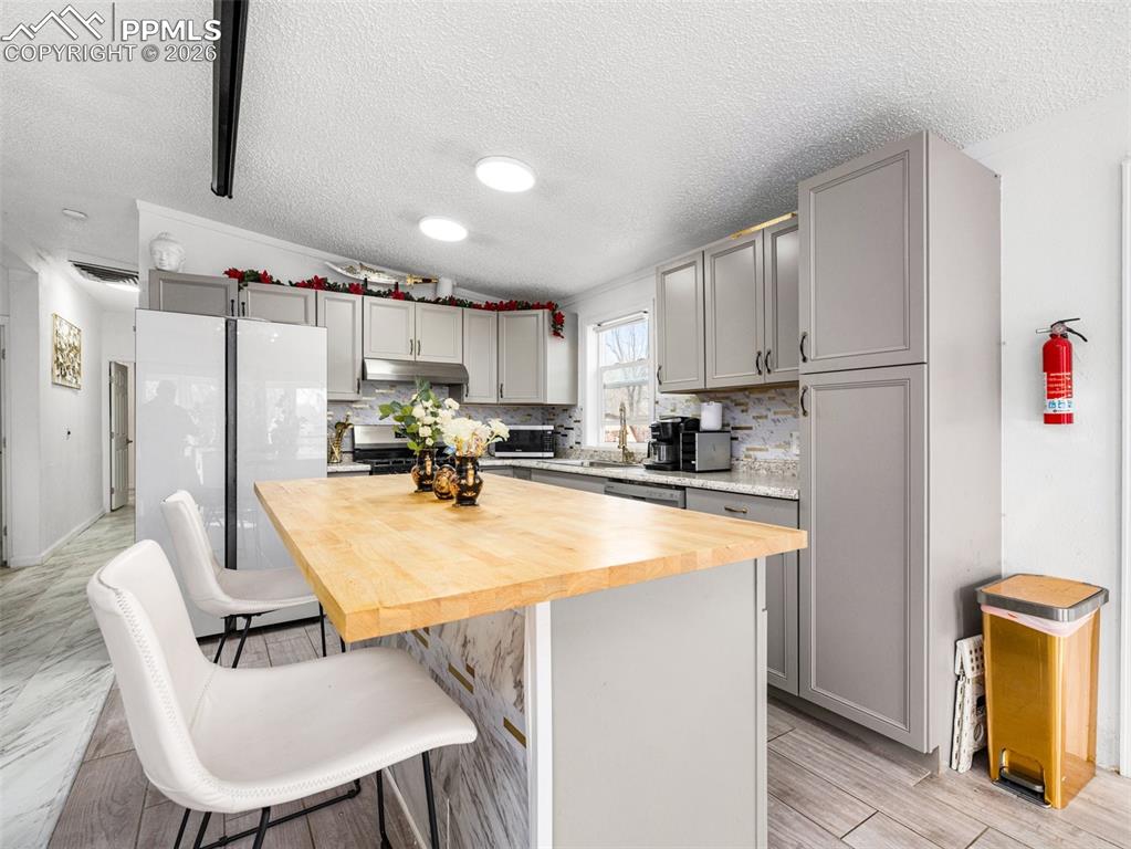 Image 14 of 29: Kitchen with butcher block countertops, gray cabinetry, decorative backspla