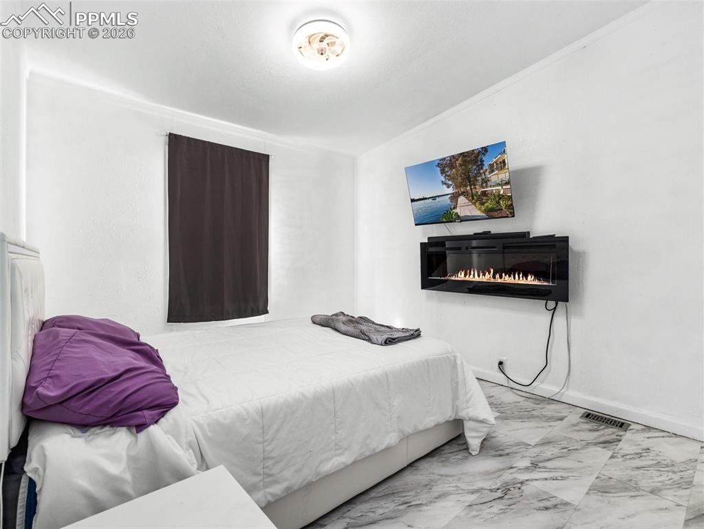 Image 24 of 29: Bedroom featuring marble look tiles and a glass covered fireplace