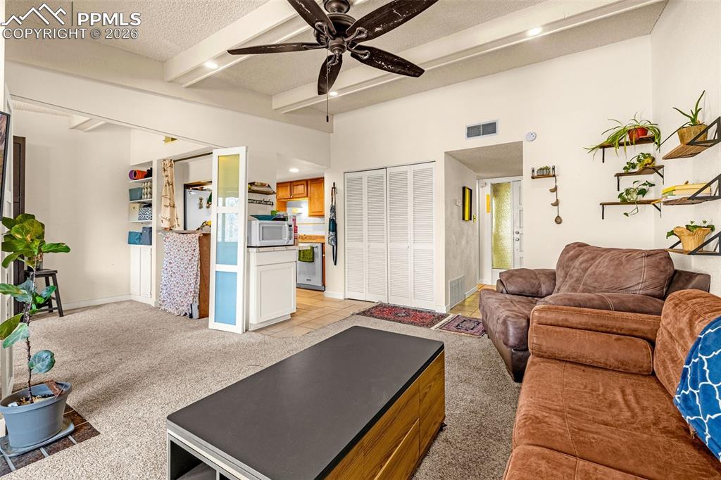 Image 11 of 29: Living room with light carpet, beamed ceiling, ceiling fan, a textured ceil