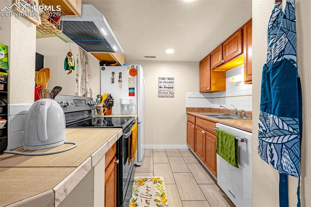 Image 12 of 29: Kitchen featuring light countertops, white appliances, exhaust hood, backsp
