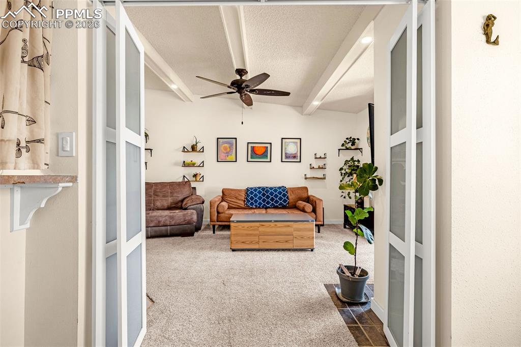 Image 5 of 29: Carpeted living area featuring a ceiling fan, a textured ceiling, and beame