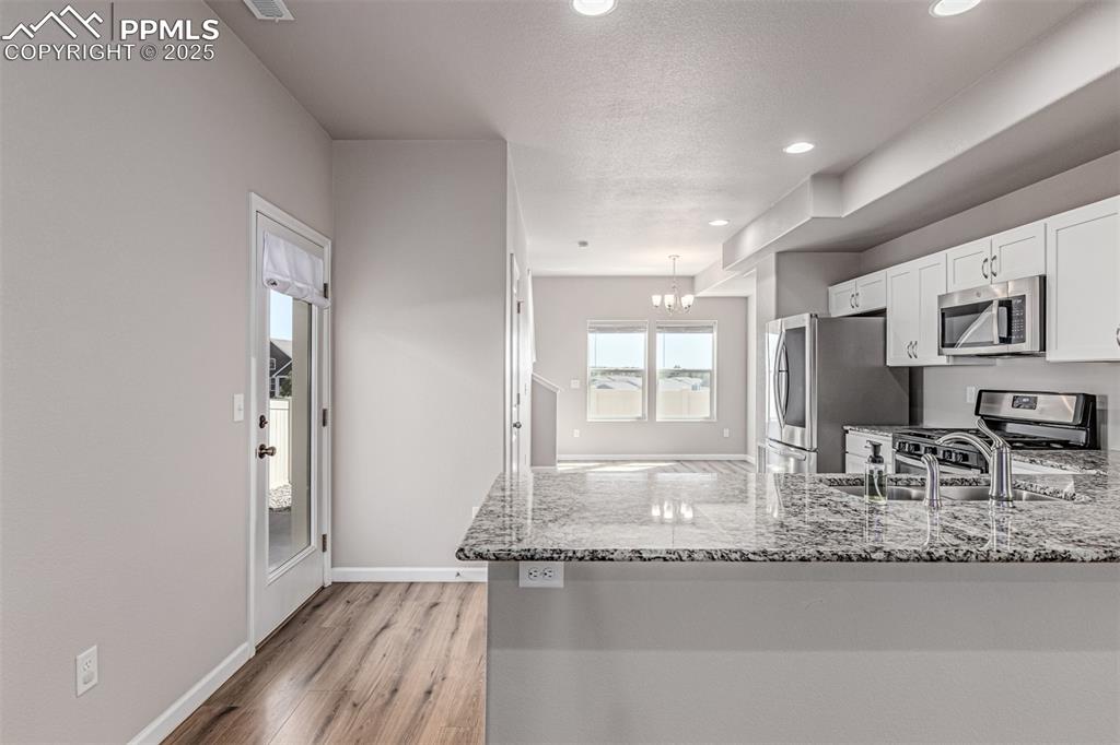 Image 8 of 29: Kitchen with white cabinetry, stainless steel appliances, light stone count