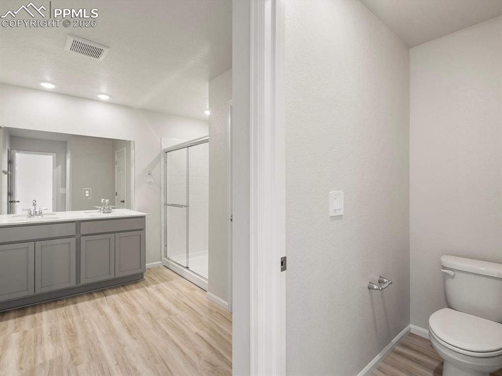 Image 25 of 30: Bathroom with light wood-style flooring, a shower stall, and double vanity