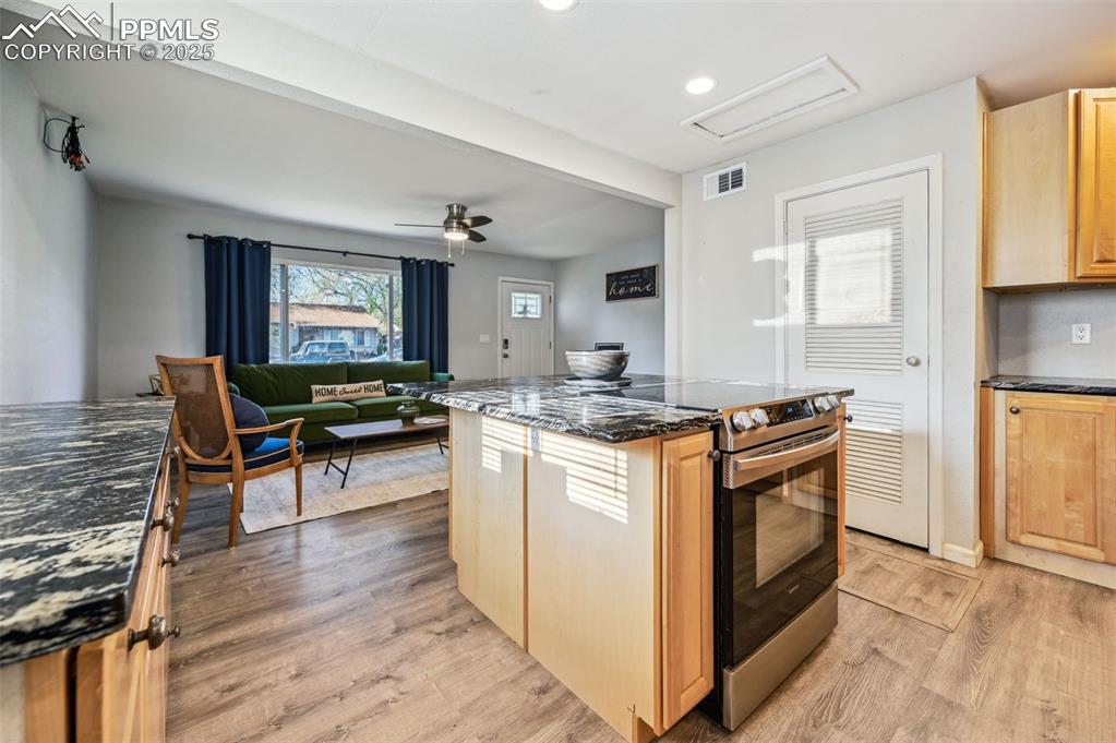 Image 10 of 27: Kitchen with light brown cabinets, dark stone countertops, ceiling fan, ele