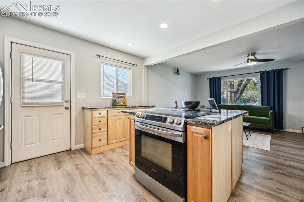 Image 7 of 27: Kitchen with electric stove, light brown cabinets, a kitchen island, dark s