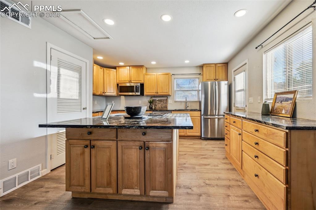Image 9 of 27: Kitchen featuring dark stone countertops, a center island, light wood-type 