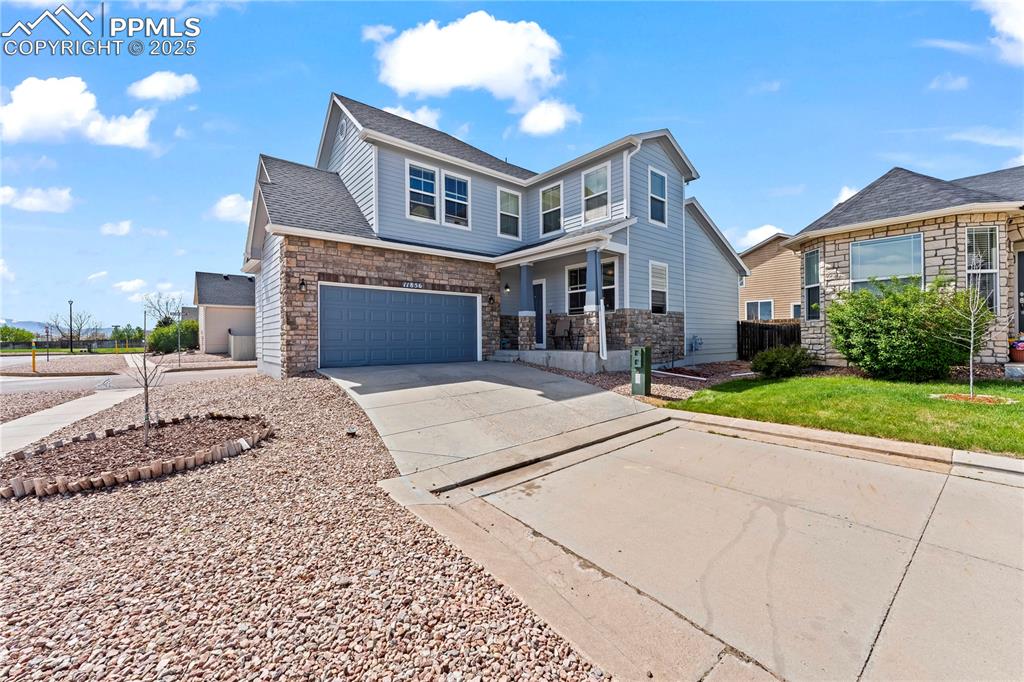 Caption: View of front facade featuring driveway, stone siding, a shingled roof, and a garage