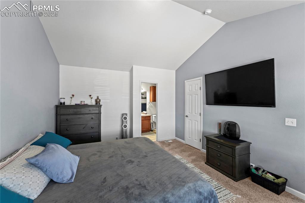Image 22 of 25: Bedroom featuring carpet floors, vaulted ceiling, and ensuite bathroom