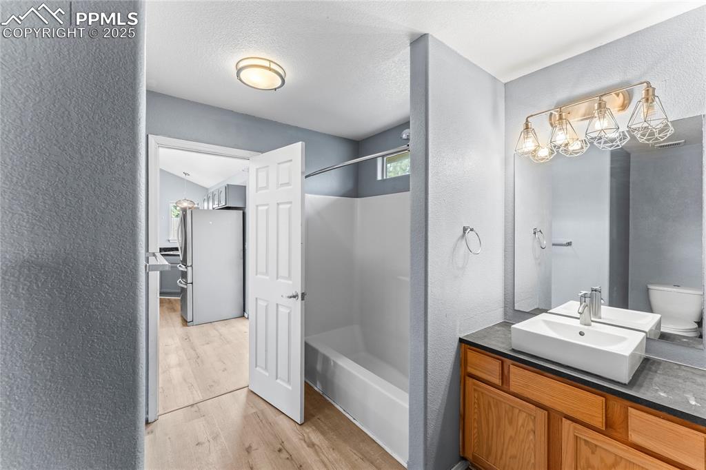 Image 17 of 37: Bathroom with a textured wall, wood finished floors, vanity, and shower / b