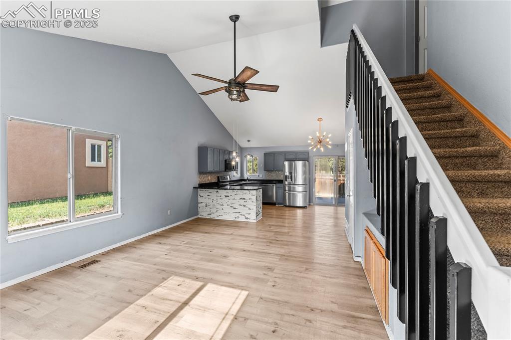 Image 8 of 37: Unfurnished living room with high vaulted ceiling, a ceiling fan, a chandel