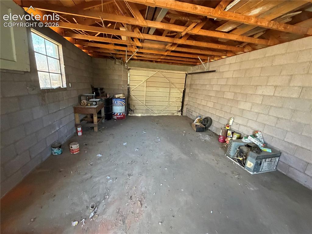 Image 24 of 28: Concrete block walls, exposed wood beam ceiling, concrete flooring, and an 