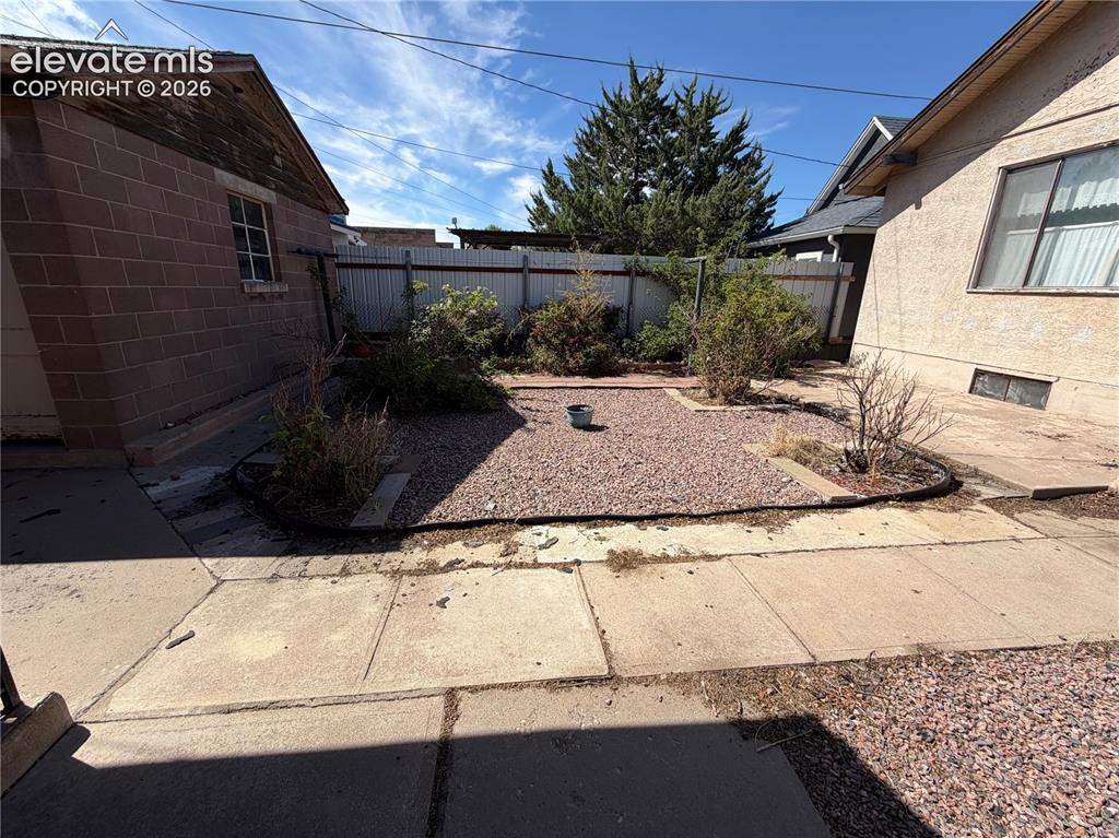 Image 26 of 28: Gravel-covered yard with a concrete block outbuilding featuring a pitched r