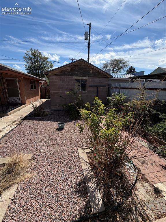 Image 27 of 28: Gravel-covered yard with a concrete block outbuilding featuring a pitched r
