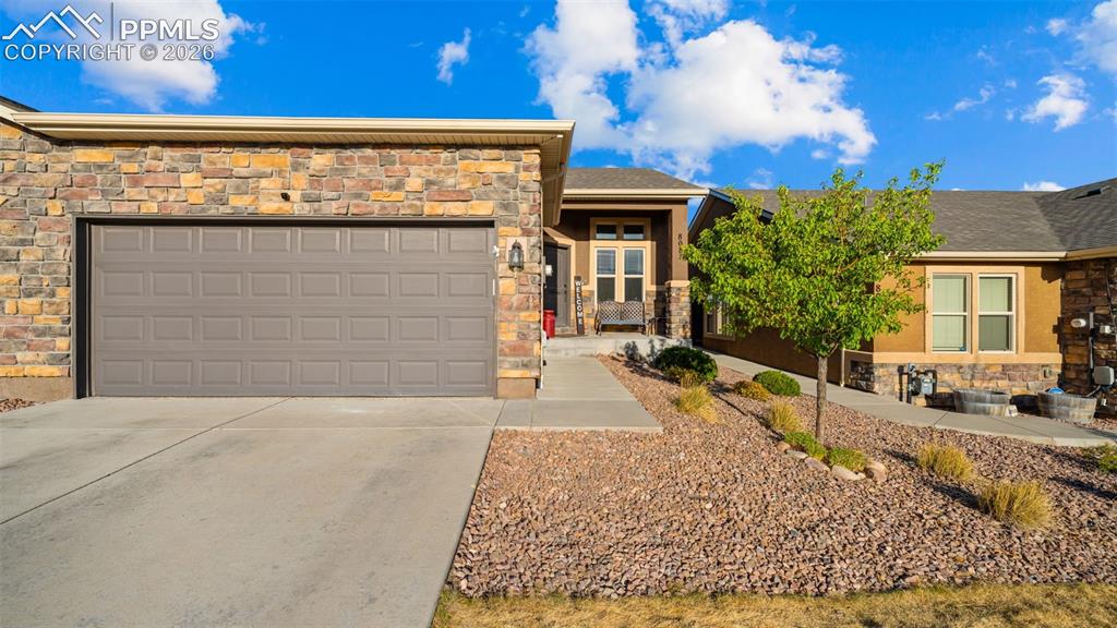 Image 1 of 27: Stone veneer facade with a two-car garage, concrete driveway, and xeriscape