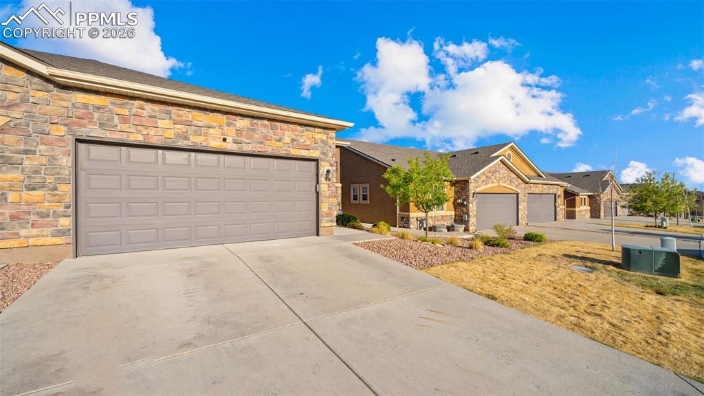 Image 2 of 27: Wide concrete driveway leading to a two-car garage with a paneled door