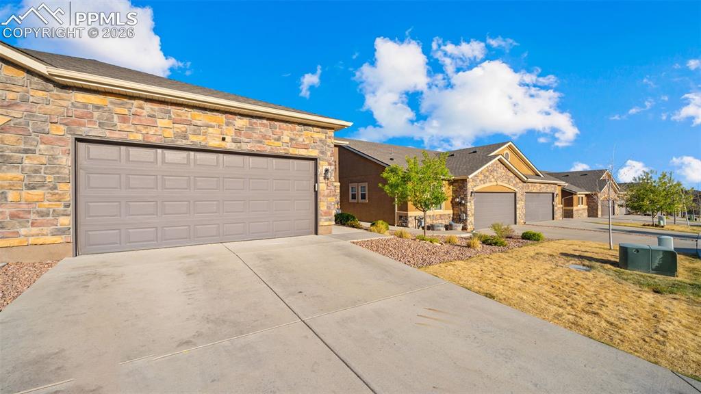 Image 2 of 27: Wide concrete driveway leading to a two-car garage with a paneled door