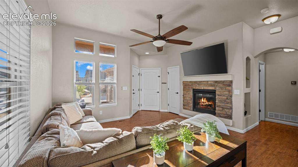 Image 6 of 27: Living room featuring a stone-clad fireplace, wood-finish flooring, a ceili