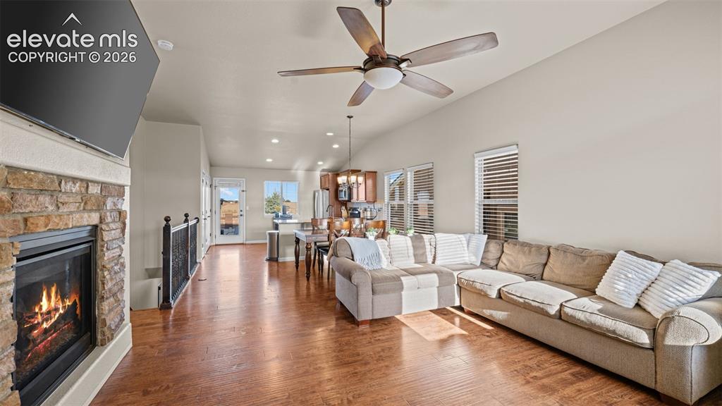 Image 7 of 27: Spacious living area featuring wood-finish flooring, a stone-clad fireplace