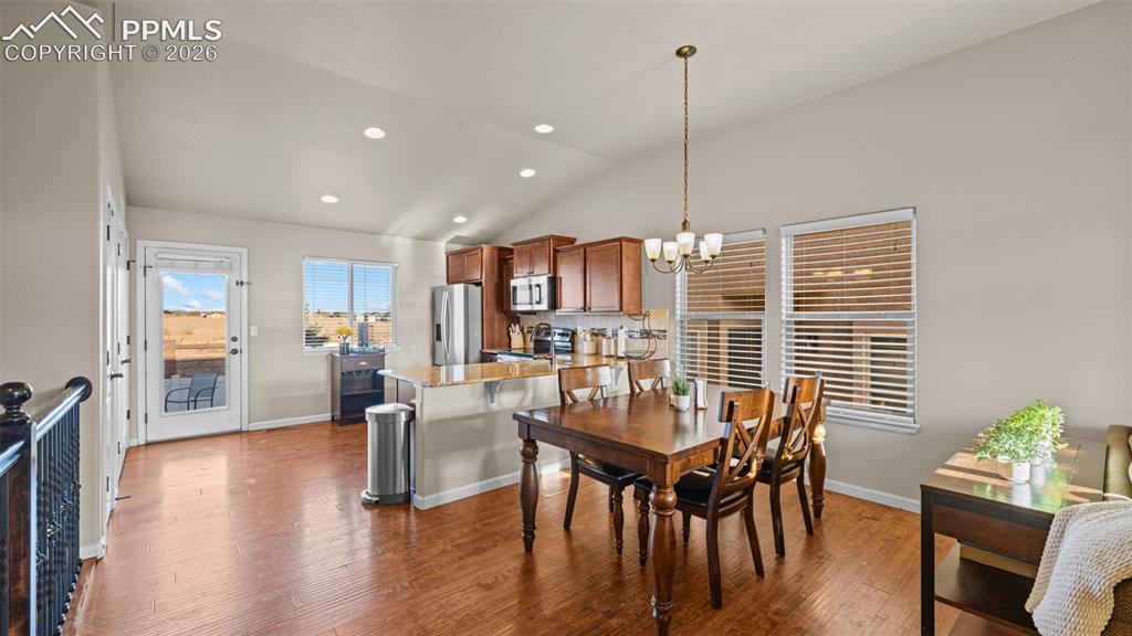 Image 8 of 27: Open-concept living space with wood-finish flooring, vaulted ceilings, and