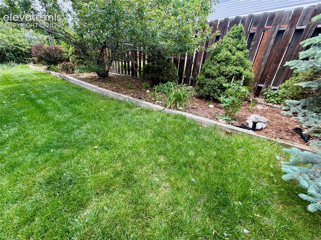 Image 10 of 49: Expansive lawn area featuring a wooden fence, diverse mature plantings, and