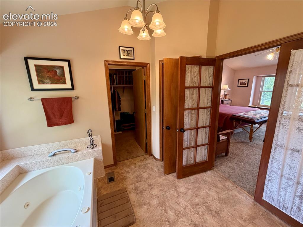 Image 30 of 49: Bathroom featuring a built-in jetted tub, light colored flooring, and a vau