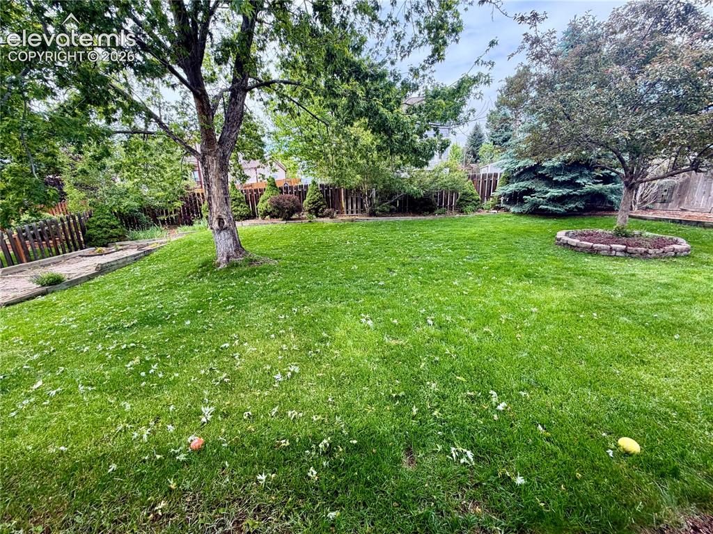 Image 8 of 49: Spacious lawn featuring mature trees, a stone-edged tree ring, and wooden f