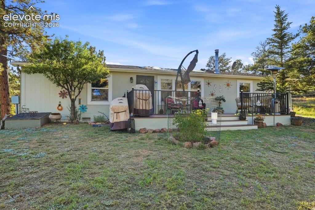 Image 11 of 50: Rear exterior featuring a single-level deck with black railing, mature land