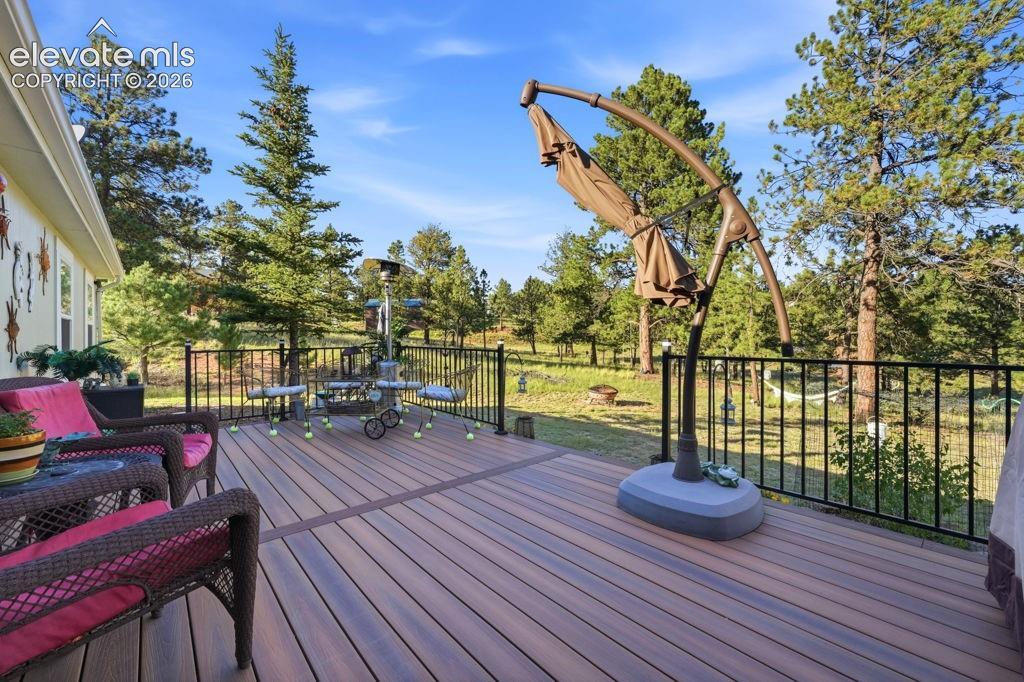 Image 17 of 50: Expansive wood-finish deck with black metal railings, bordered by mature ev