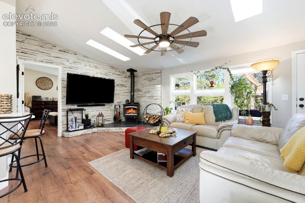 Image 19 of 50: Vaulted ceiling with skylights, wood-finish flooring, accent wall, wood-bur