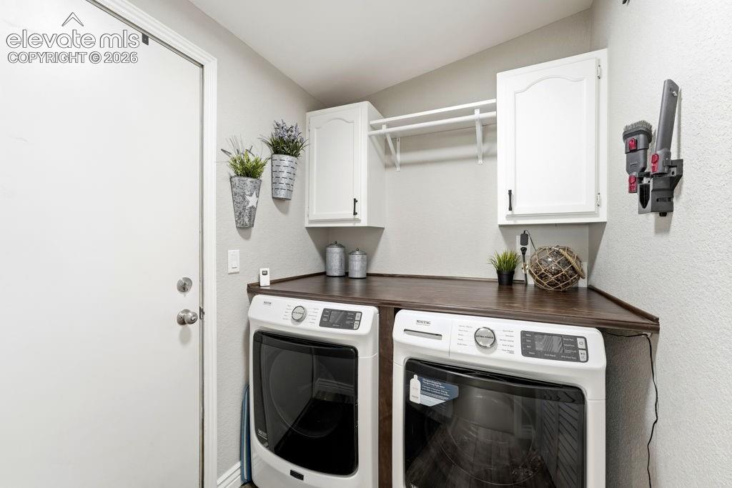 Image 31 of 50: Dedicated laundry area featuring white cabinetry, a dark wood-finish counte