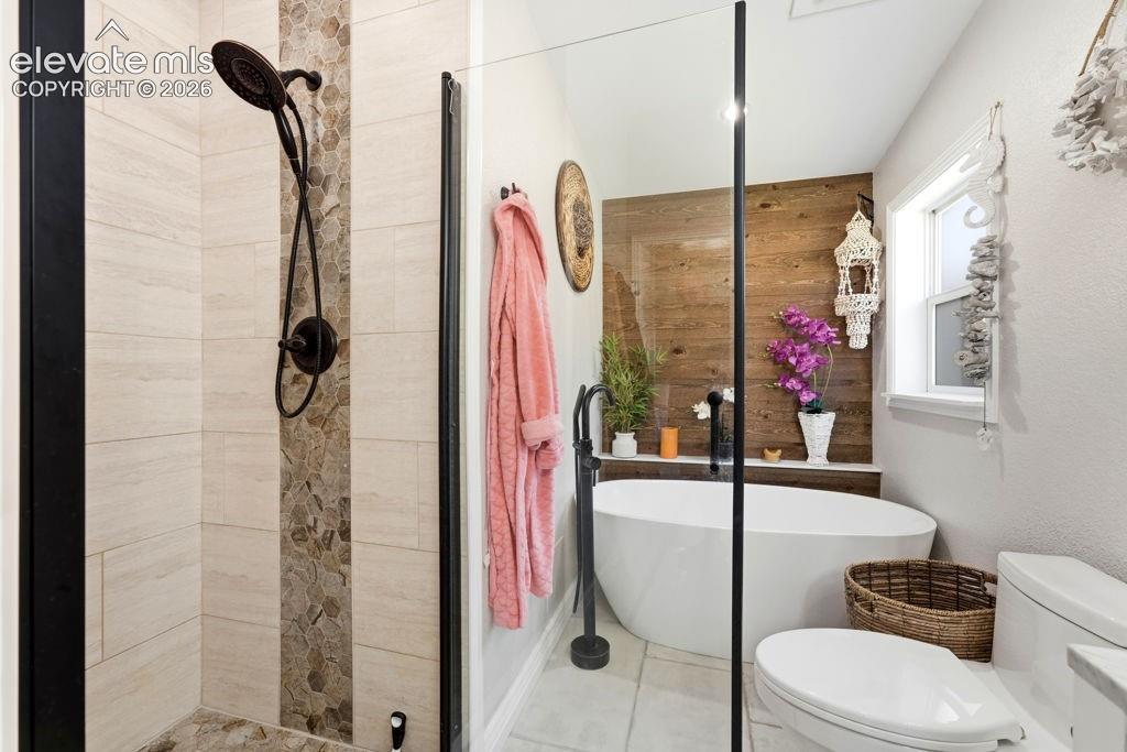 Image 35 of 50: Freestanding soaking tub with a floor-mounted faucet, wood-finish accent wa