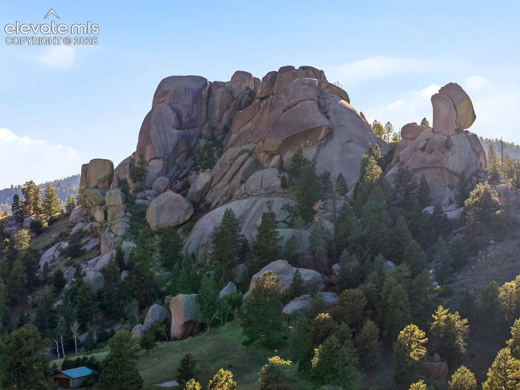 Image 47 of 50: Rocky terrain with dense evergreen trees and a prominent natural rock forma