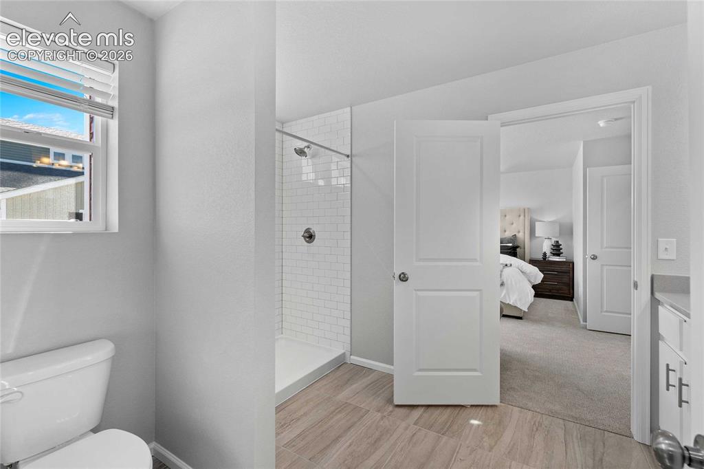 Image 13 of 25: Wood-finish flooring, white subway tile shower, white paneled doors, and a 