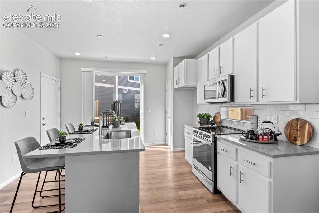 Image 7 of 25: Bright kitchen with wood-finish flooring, white cabinetry, a built-in micro