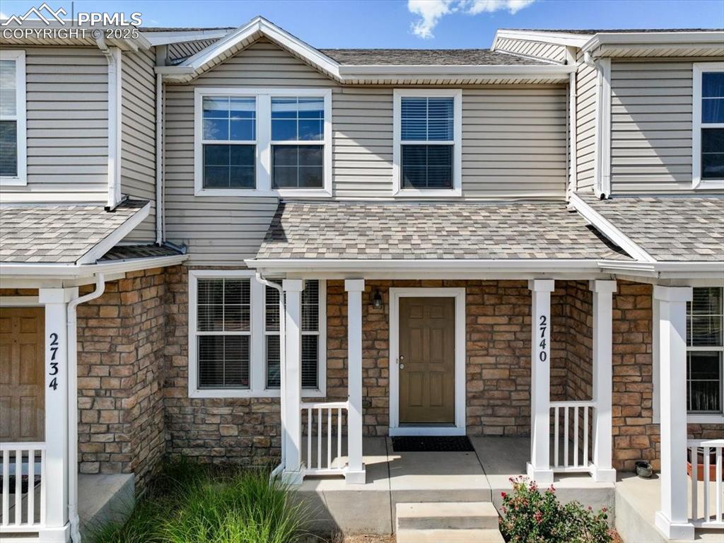 Caption: View of front of home featuring stone siding, a porch, and roof with shingles
