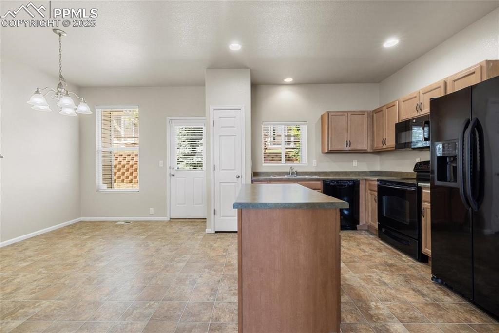 Image 12 of 42: Kitchen featuring black appliances, a center island, decorative light fixtu