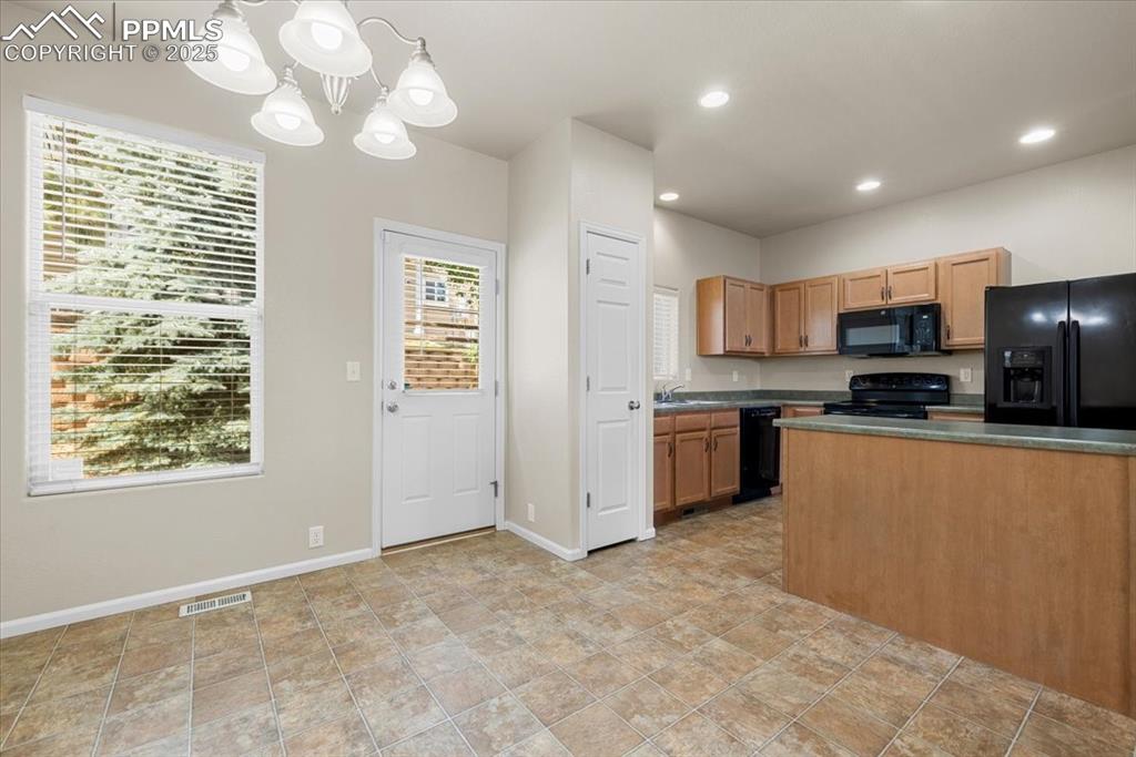 Image 13 of 42: Kitchen featuring dark countertops, black appliances, decorative light fixt
