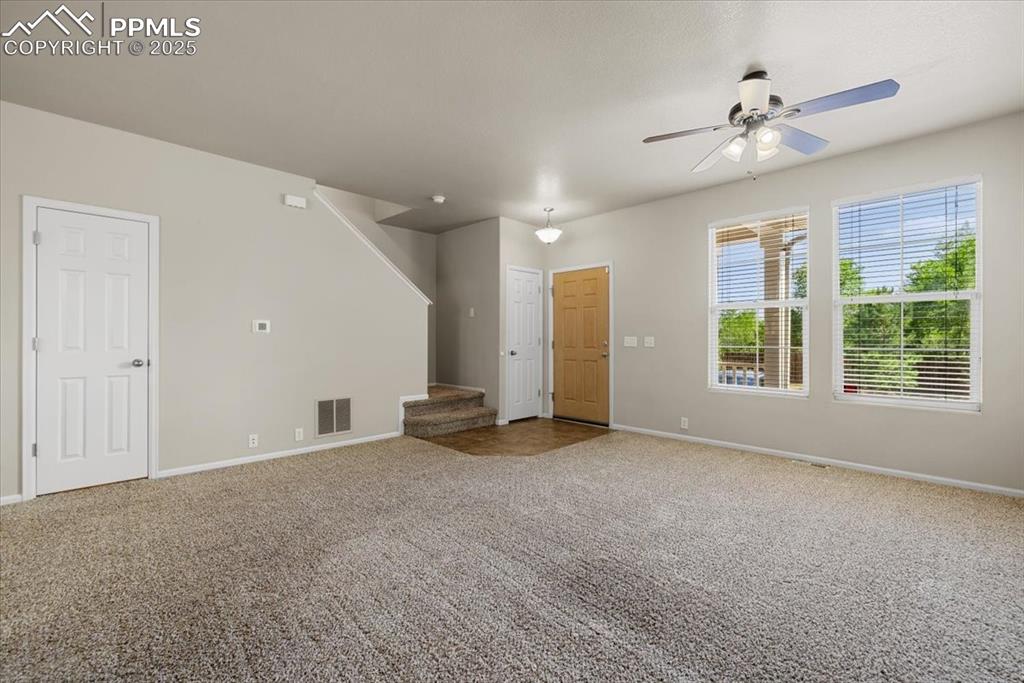 Image 6 of 42: Unfurnished living room featuring carpet, stairs, and a ceiling fan