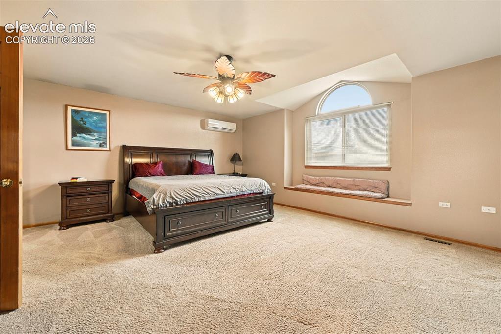 Image 19 of 50: Primary bedroom with ceiling fan, arched window, window bench, wall-mounted