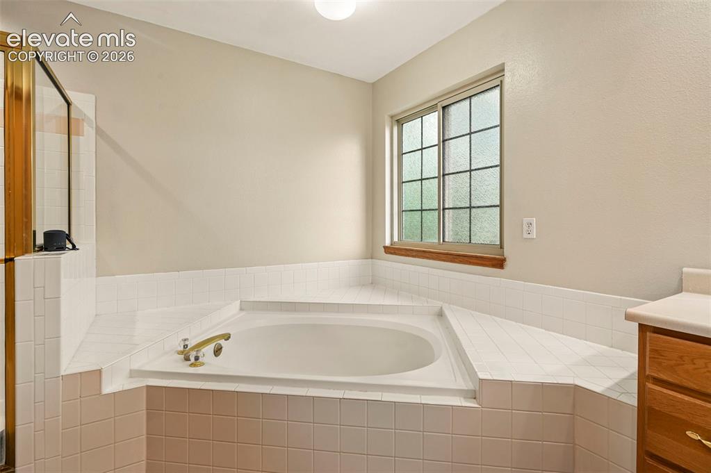 Image 22 of 50: Built-in soaking tub with deck tiling, brass fixtures, and an adjacent show